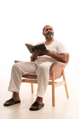 النظر الى شيء ما، هواية القراءة والاستكشاف، مفهوم التثقيف والبحث العلمي، قضاء وقت الفراغ بالتعلم والثقافة، بورتريه لرجل عربي سعودي خليجي يرتدي سروال وفانيلا أبيض يجلس على كرسي يقرأ كتاب، خلفية بيضاء