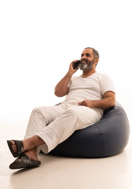 Making a phone call via mobile, expressions of happiness and joy, a portrait of an Arab Saudi Gulf man wearing white pants and a t-shirt sitting on a chair with a bag, holding a mobile phone in his hands, white background.