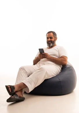 Browsing social media on mobile, expressions of happiness and joy, a portrait of an Arab Saudi Gulf man wearing white pants and a t-shirt sitting on a chair between bags holding a mobile phone in his hands, white background.