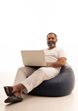 تصفح برامج التواصل الاجتماعي, عقد إجتماع عمل عبر الإنترنت، إستخدام الحاسوب المحمول لإنجاز المهام،  بورتريه لرجل عربي سعودي خليجي يرتدي سروال وفانيلا أبيض يجلس على كرسي بين باج يحمل جهاز اللابتوب، تطور التكنولوجيا والأجهزة التقنية، خلفية بيضاء