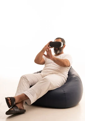 The reference to a place with expressions of integration and simulation of the imaginary world, an attempt to click on something, a portrait of an Arab Saudi Gulf man wearing white pants and a t-shirt sitting on a chair between a bag placing 3D glasses, raising his index finger upwards, white background.