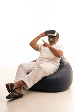 الاشارة الى مكان ما بتعابير الاندماج ومحاكاة العالم الخيالي، محاولة النقر على شيء ما,  بورتريه لرجل عربي سعودي خليجي يرتدي سروال وفانيلا أبيض يجلس على الاريكة تضع نظارة ثلاثية الأبعاد يقوم برفع اصبع السبابة للاعلى, خلفية بيضاء