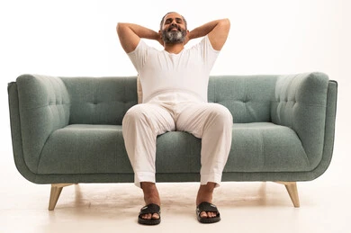 ايماءات تدل على الراحة، مفهوم الاسترخاء والاستمتاع بالأجواء الهادئة، بورتريه لرجل عربي سعودي خليجي يرتدي سروال وفانيلا أبيض يجلس على الاريكة ويضع يديه تحت رأسه، الشعور بالتعب والحاجة إلى النوم، خلفية بيضاء