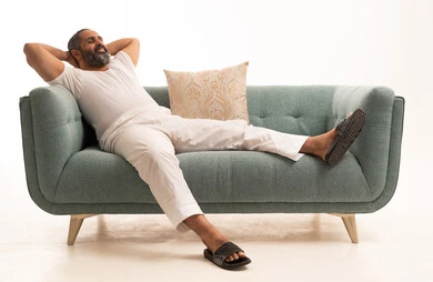 مفهوم الاسترخاء والاستمتاع بالأجواء الهادئة، بورتريه لرجل عربي سعودي خليجي يرتدي سروال وفانيلا أبيض يجلس على الاريكة ويضع يديه تحت رأسه، الشعور بالتعب والحاجة إلى النوم، ايماءات تدل على الراحة، خلفية بيضاء