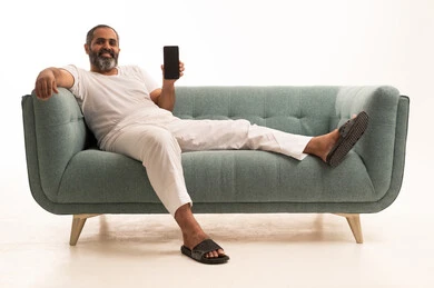 A display of a blank black screen, the use of modern technologies, the quality of mobile applications and services, a portrait of an Arab Saudi Gulf man wearing white pants and a t-shirt sitting on a sofa looking at the camera with gestures of joy, white background.