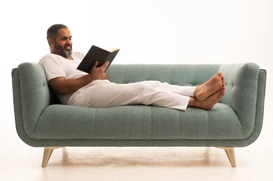 استغلال الوقت في التثقف، مفهوم التمعن والتركيز، مفهوم محو الأمية والتعلم، التخطيط المستقبلي للأهداف والطموحات, بورتريه لرجل عربي سعودي خليجي يرتدي سروال وفانيلا أبيض يجلس على الاريكة  ويمسك بيديه كتاب يقرأه بتمعن, خلفية بيضاء