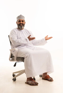 حركة يد واشارات رفع وحمل عنصر ما،  بورتريه لرجل عربي خليجي عماني يرتدي الدشداشة و الكمة يجلس على الكرسي ينظر الى الكاميرا بايماءات السرور والسعادة ويشير نحو مكان ما، التحية والترحيب واستقبال شخص ما، خلفية بيضاء