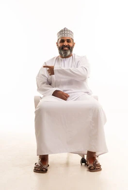 الاشارة نحو شيء وتحديد هدف ما، بورتريه لرجل عربي خليجي عماني يرتدي الدشداشة و الكمة يجلس على الكرسي يشير باصبع السبابة الى الجانب، خلفيه بيضاء الاشارة نحو شيء وتحديد هدف ما، بورتريه لرجل عربي خليجي عماني يرتدي الدشداشة و الكمة يجلس على الكرسي يشير باصبع السبابة الى الجانب، خلفيه بيضاء