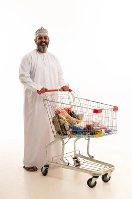 Getting the necessary essentials, benefiting from discounts on products, enjoying shopping in malls and commercial centers, a portrait of an Arab Gulf Omani man wearing a dishdasha and kumma pulling a shopping cart in front of him, full body, white background.