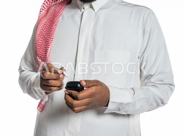 بورتريه بصورة مقربة لرجل عربي خليجي سعودي ، يحمل سماعة لاسليكة ، خلفية بيضاء ، سماعة أذن لاسليكة ، مفهوم إستخدام إكسسوارات خاصة بالأجهزة التقنية الحديثة