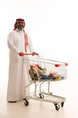 شراء المستلزمات والحاجيات الضرورية، الاستفادة من الخصومات على المنتجات، الاستمتاع بالتسوق في المولات والمراكز التجارية، بورتريه لرجل عربي خليجي سعودي يرتدي الشماغ والثوب التقليدي يجر عربة التسوق أمامه، الجسم بالطول الكامل، خلفية بيضاء