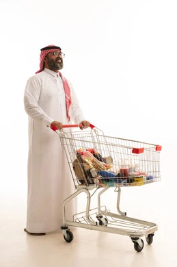 الاستفادة من الخصومات على المنتجات، الاستمتاع بالتسوق في المولات والمراكز التجارية، شراء المستلزمات والحاجيات الضرورية، بورتريه لرجل عربي خليجي سعودي يرتدي الشماغ والثوب التقليدي يجر عربة التسوق أمامه، الجسم بالطول الكامل، خلفية بيضاء