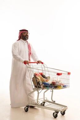 الاستمتاع بالتسوق في المولات والمراكز التجارية، الاستفادة من الخصومات على المنتجات، شراء المستلزمات والحاجيات الضرورية، بورتريه لرجل عربي خليجي سعودي يرتدي الشماغ والثوب التقليدي يجر عربة التسوق أمامه، الجسم بالطول الكامل، خلفية بيضاء