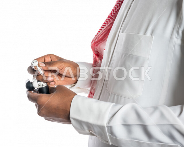 بورتريه بصورة مقربة لرجل عربي خليجي سعودي ، يحمل سماعة لاسليكة ، خلفية بيضاء ، سماعة أذن لاسليكة ، مفهوم إستخدام إكسسوارات خاصة بالأجهزة التقنية الحديثة