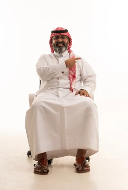 مد اليد للاشارة الى شيء ما بواسطة إصبع السبابة، شد الإنتباه ولفت النظر، ايماءات سعادة وفرح،  بورتريه لرجل عربي خليجي سعودي يرتدي الشماغ والثوب التقليدي يجلس على كرسي، خلفيه بيضاء