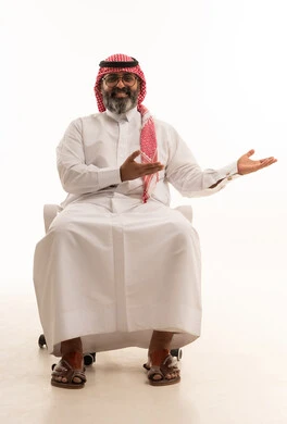 الإشارة إلى عنصر ما, التوضيح والدلالة لمكان محدد, بورتريه لرجل عربي خليجي سعودي يرتدي الشماغ والثوب التقليدي يجلس على كرسي يشير بيدية على الجانب، تحديد موقع شيء معين، خلفية بيضاء