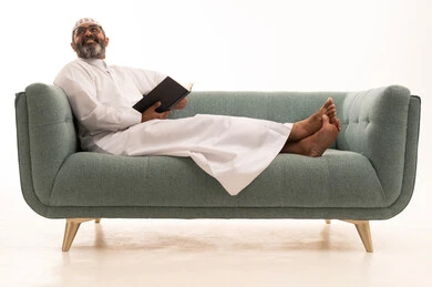 Looking at something, the hobby of reading and exploration, spending free time learning and culture, the concept of education and scientific research, a portrait of an Arab Gulf Saudi man wearing a white thobe and a headscarf sitting on a sofa holding a book, gestures of engagement and focus, white background.
