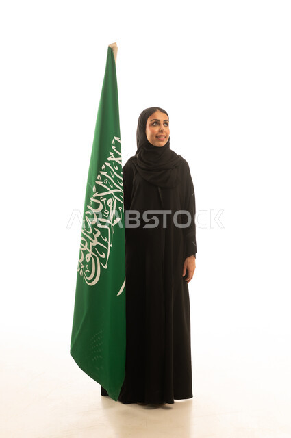 بورتريه خلفية بيضاء لامرأة سعودية محجبة عربية خليجية ترتدي عباءة سوداء تمسك العلم السعودي  ,النظر الى شئ ما ,الجسم بالطول الكامل