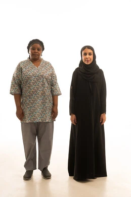 الوقوف جنبًا الى جنب والنظر للكاميرا ,امرأة عربية خليجية سعودية محجبة ترتدي عباءة سوداء ,عاملة منزلية افريقية سمراء البشرة ترتدي يونيفورم اللون الرمادي ,بورتريه خلفية بيضاء الجسم بالطول الكامل