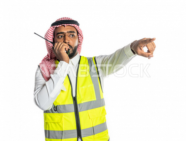 بورتريه لمهندس عربي خليجي سعودي ، يرتدي الزي السعودي التقليدي وسترة الحماية خاصة بالعمل ، يستخدم جهاز اتصال لاسلكي ، يحمل بيده تقارير ، الإشراف ومتابعة العمل ، إعطاء أوامر خاصة بالعمل ، مهن و وظائف هندسية ، ادارة المشاريع المعمارية الهندسية ، خلفية بيضاء