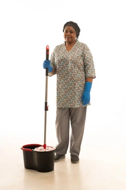 القيام بالاعمال المنزلية اليومية بسهولة باستخدام الادوات اللازمة لها ,بورتريه خلفية بيضاء الجسمبالطول الكامل لعاملة منزلية افريقية سمراء البشرة ترتدي يونيفورم باللون الرمادي تمسك ممسحة للارضيات يدوية ,النظر للكاميرا