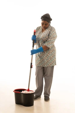 اعمال النظافة والتعقيم اليومية للمنزل ,عامل منزلية افريقية سمراء البشرة ترتدي يونيفورم رمادي اللون تقوم بمسح الارض باستخدام الممسحة اليدوية ,بورتريه خلفية بيضاء الجسم بالطول الكامل
