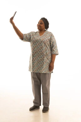 التقاط سيلفي باستخدام الهاتف المحمول ,بورتريه خلفية بيضاء الجسم بالطول الكامل لعاملة منزلية افريقية سمراء اليشرة ترتدي يونيفورم باللون الرمادي