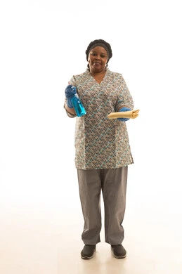 النظر للكاميرا بابتسامة ,عاملة منزلية افريقية سمراء البشرة ترتدي قفازات جلدية زرقاء ويونيفورم لون رمادي تحمل بخاخ لتلميع وتعقيم الزجاج ,بورتريه خلفية بيضاء الجسم بالطول الكامل