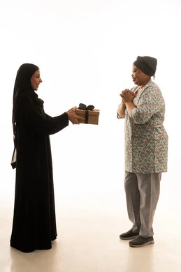 الشكر والعرفان لخدمات العمالة الاجنبية ,بورتريه خلفية بيضاء لامرأة عربية خليجية سعودية محجبة ترتدي عباءة سوداء تقدم هدية لعاملة منزلية سمراء البشرة افريقية ترتدي يونيفورم لون رمادي ,الجسم بالطول الكامل