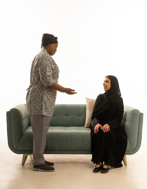 مناقشة اعمال المنزل الروتينبة في جو من الود و التفاهم ,بورتريه خلفية بيضاء لامرأة عربية خليجية سعودية محجبة ترتدي عباءة سوداء ,عاملة منزلية افريقيةسمراء البشرة ترتدي يونيفورم باللون الرمادي ,الجسم بالطول الكامل