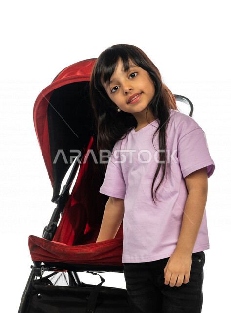 Portrait of a Saudi Arabian Gulf girl standing next to the stroller with gestures indicating happiness and love, brotherhood bond, emotional bonding, happy family concept, family picnic and tour, spending fun family times