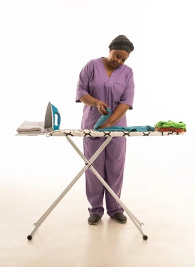 African domestic worker wearing a purple uniform; full-body portrait against a white background of a dark-skinned maid organizing and arranging clothes.