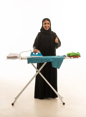 A veiled Saudi Arabian woman wearing a black abaya gives a thumbs-up gesture of approval. A full-body portrait against a white background depicts a Saudi woman ironing clothes.