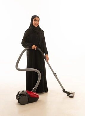 بورتريه خلفية بيضاء لامرأة سعودية عربية خليجية ترتدي عباءة سوداء خليجية بنظرة أمامية وابتسامة للكاميرا,استخدام المكنسة الكهربائية في الاعمال المنزلية