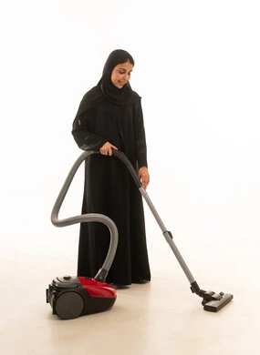 بورتريه  امراة عربية سعودية خليجية ترتدي عباءة سوداء تقليدية تقوم بأعمال النظافة  المنزلية  الروتينية ,استخدام التقنيات الحديثة في الاعمال المنزلية باستخدام المكنسة الكهربائية , خلفية بيضاء