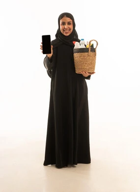 بورتريه باتجاه الكاميرا لامرأة عربية سعودية خليجية محجبة ترتدي عباءة سوداء تحمل بيدها الهاتف المحمول ,عرض شاشة سوداءفارغة مستلزمات التنظيف عبر الجوال ,خلفية بيضاء