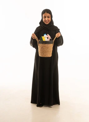 بورتريه  لامرأة عربية سعودية خليجية ترتدى عباءة خليجية سوداء تحمل سلة من القش مليئة بادوات التنظيف