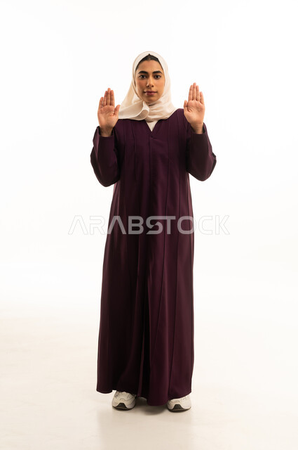 حماية النفس من ضرر خارجي, القلق والاحتياط والابتعاد عن شيء ما، رفع اليدين بإيماءات التوقف وعدم الاقتراب, بورتريه لامرأه خليجيه سعوديه تقف بحذر وذعر ورهبة،  الجسم بالطول الكامل, خلفية بيضاء