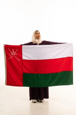 الاحتفال بذكرى اليوم الوطني العماني 18 نوفمبر, النظر الى شىء ما, بورتريه لإمرأة عربية خليجية عمانية محجبة ترتدي العباءة الملونة تضع  العلم الوطني للبلاد على كتفها، حب الوطن والانتماء إليه, احياء ذكرى تأسيس الدولة 1775 م , الجسم بالطول الكامل، خلفية بيضاء