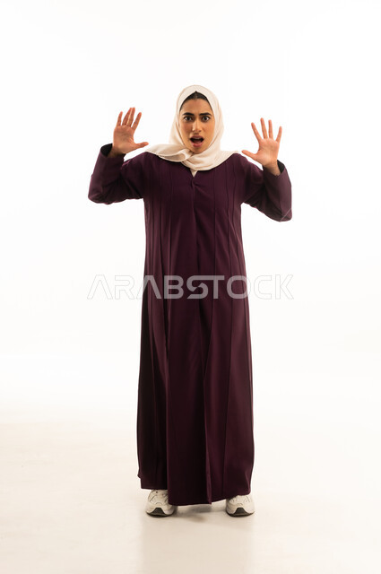 الشعور بالصدمة و الدهشة والتعجب والذهول , بورتريه لإمرأة خليجية سعودية محجبة ترتدى العباءة ترفع يديها للأعلى بتعابير التفاجؤ عند رؤية شيء ما, الجسم بالطول الكامل, خلفية بيضاء