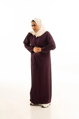 إيماءات التقيؤ والغثيان، الإحساس بالمغص والوجع، الشعور بحرقة في المعدة، الحاجه للمساعدة وطلب العلاج, بورتريه لإمرأة خليجية سعودية محجبة ترتدى العباءة  تضع يدها على بطنها تنحني من شدة الألم, الجسم بالطول الكامل, خلفية بيضاء