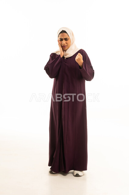 وجع اللثه وتسوس الأضراس، طلب العلاج و المساعده، الحاجه لزيارة الطبيب, بورتريه لإمرأة خليجية سعودية محجبة ترتدى العباءة  تضع يدها على خدها بإيماءات الشعور بألم الأسنان, الجسم بالطول الكامل, خلفية بيضاء