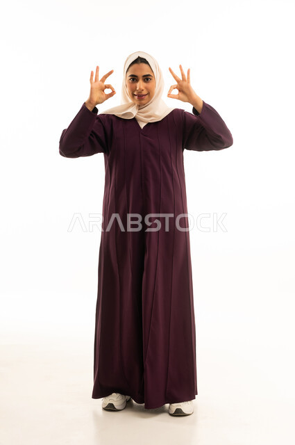علامة الجوده والإمتياز, بورتريه لإمرأه عربيه خليجيه سعودية محجبه ترتدي العباءه ترفع يديها بإيماءات تدل على الإعجاب والرضى، مفهوم القبول والموافقه , تعابير السرور والسعادة،, الجسم بالطول الكامل, خلفية بيضاء
