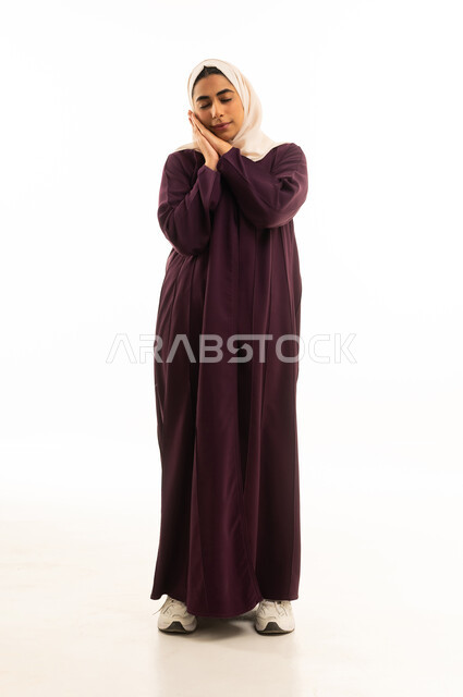 النعاس والتعب و الارهاق، السهر لوقت متأخر من الليل, بورتريه لإمرأه عربيه خليجيه سعودية محجبه ترتدي العباءه  تضع يديها تحت رأسها بإيماءات الخمول والكسل, الجسم بالطول الكامل, خلفية بيضاء