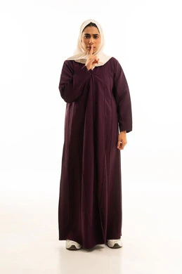 التوقف عن الكلام و الأمر بالصمت و الاستماع، بورتريه لإمرأة عربية خليجية محجبة ترتدي العباءة والحجاب تنظر إلى الكاميرا وترفع اصبعها الى فمها, الجسم بالطول الكامل, خلفية بيضاء