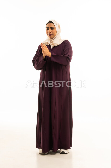 A portrait of a Saudi Arabian Gulf woman wearing a hijab, raising her hands in humility and supplication, seeking help and expressing a desire to fulfill wishes, standing with gestures of prayer, pleading, and seeking mercy, full-body, with a white background.