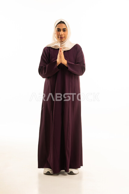 الوقوف بإيماءات الدعاء والتوسل والاسترحام, بورتريه لامرأة عربية خليجية سعودية محجبة ترفع يديها بخشوع واستعطاف, طلب العون والرغبة في تحقيق الأمنيات, الجسم بالطول الكامل, خلفية بيضاء