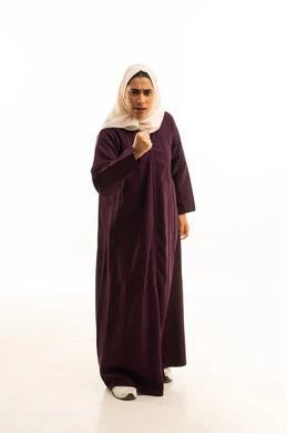 بورتريه لامرأة عربية خليجية سعودية محجبة ترتدي عباءة ترفع قبضة يديها للإستعداد لتصدي القتال، إيماءات وجه ويدين تدل على المنافسة والتحدي، الجسم بالطول الكامل, خلفية بيضاء