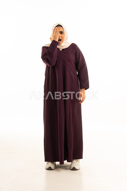 Expressions of shyness and modesty, suddenly remembering something, a portrait of a Saudi Arabian Gulf woman wearing a hijab and an abaya, covering one eye with her hand, gestures of astonishment and surprise, taking a quick glance at a situation, white background.