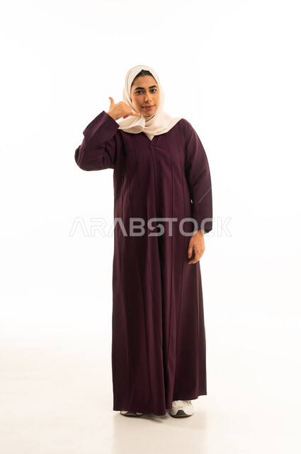 إشارة تعني إتصل بي , التواصل مع الأصدقاء,  بورتريه لامرأة عربيه خليجيه سعوديه محجبه ترتدي العباءة تقوم بإيماءات وجه ويدين تدل على إجراء مكالمه هاتفيه، الجسم بالطول الكامل, خلفية بيضاء